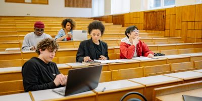 Group of college students studying together in a classroom, focused on learning with laptops and books.
